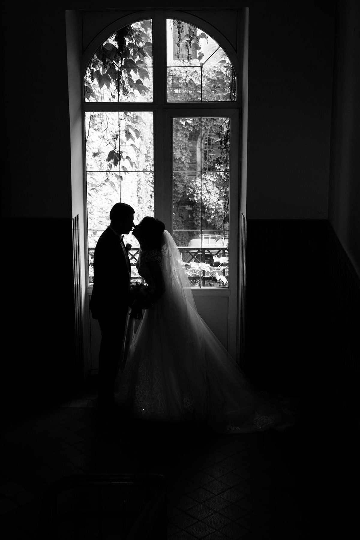 Les mariés en silhouette devant une haute fenêtre, dans la lumière